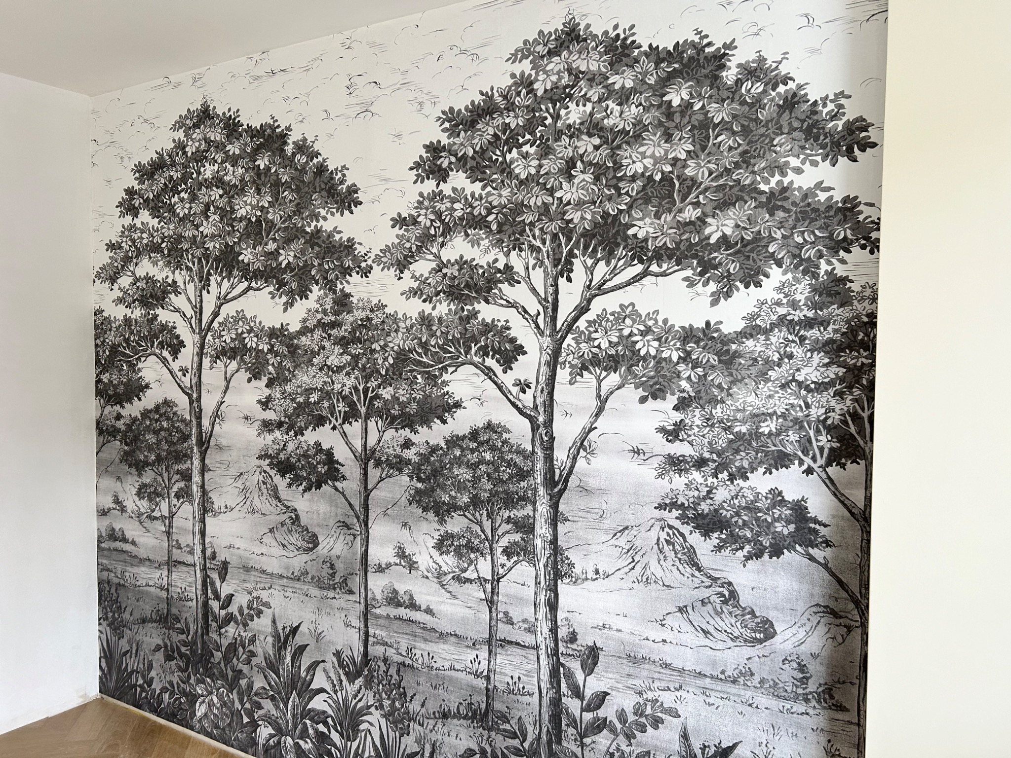 Ściana pokryta czarno-białą tapetą z motywem drzew i górskiego krajobrazu, widok z bliska na fragment wykończonego wnętrza.