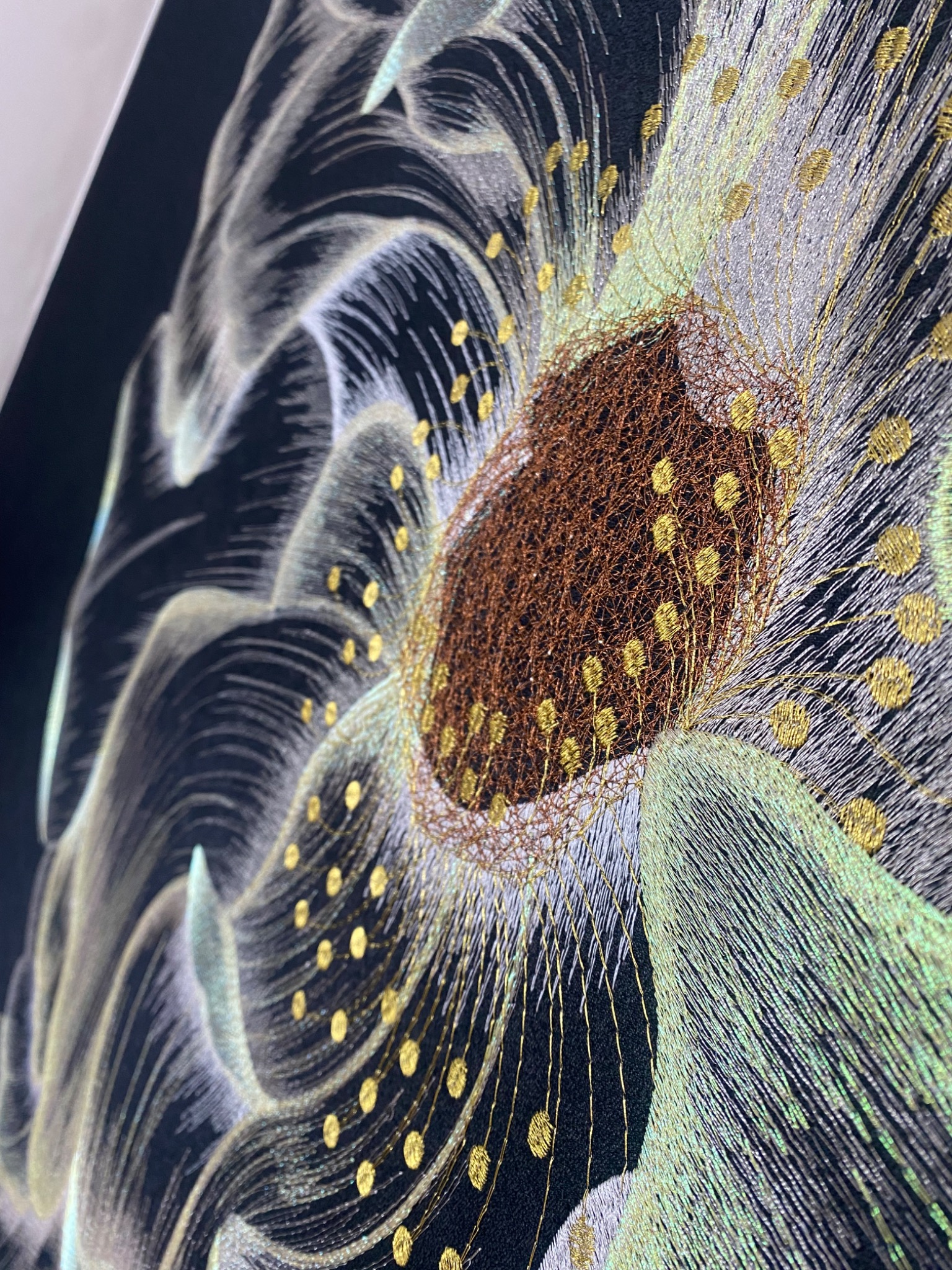 Abstrakcyjna dekoracja ścienna z motywem kwiatowym, wykonana z nici w kolorach brązu, złota, bieli i zieleni na czarnym tle, widok z boku.