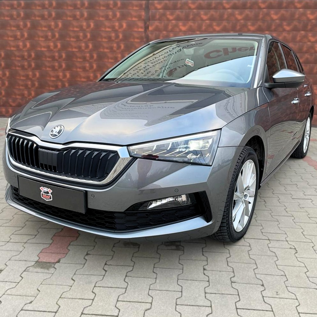 Szary samochód Skoda Scala po detailingu, widoczny z przodu na tle ceglanej ściany i kostki brukowej.