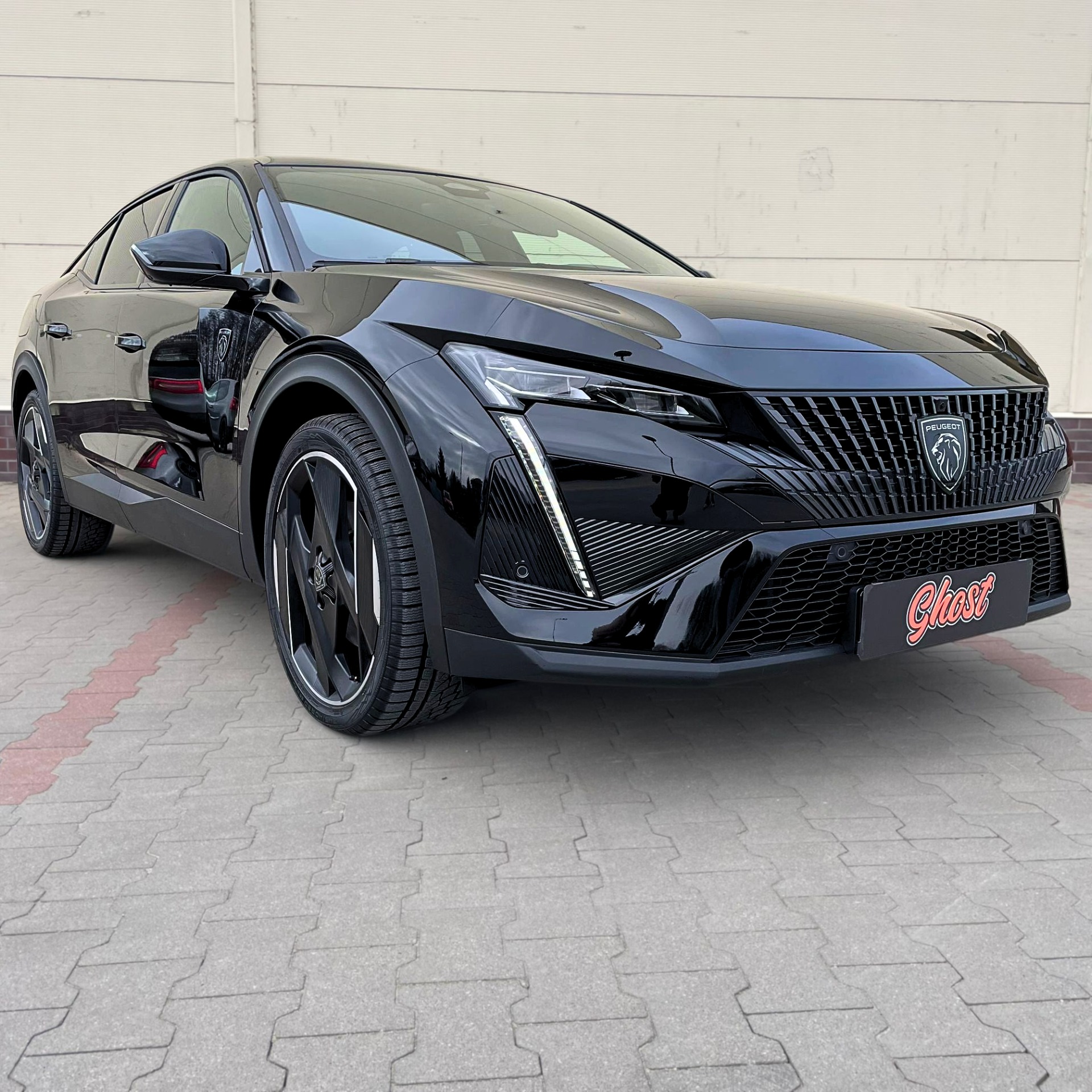 Czarny Peugeot 408 po detailingu z widocznym logo Ghost Autodetailing na tabliczce przed samochodem, prezentowany na zewnątrz na tle jasnej ściany.