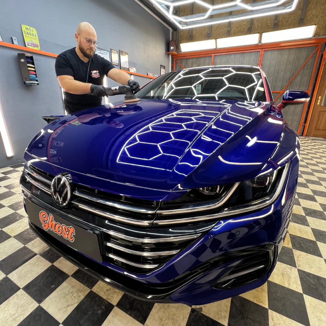 Polerowanie lakieru niebieskiego Volkswagena Arteona przy użyciu polerki elektrycznej w warsztacie z oświetleniem LED o strukturze plastra miodu.