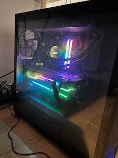 Wnętrze komputera stacjonarnego z podświetleniem RGB, widoczne chłodzenie wodne procesora, karta graficzna z podświetleniem, wentylator z logo ASUS TUF, obudowa z oknem z hartowanego szkła.