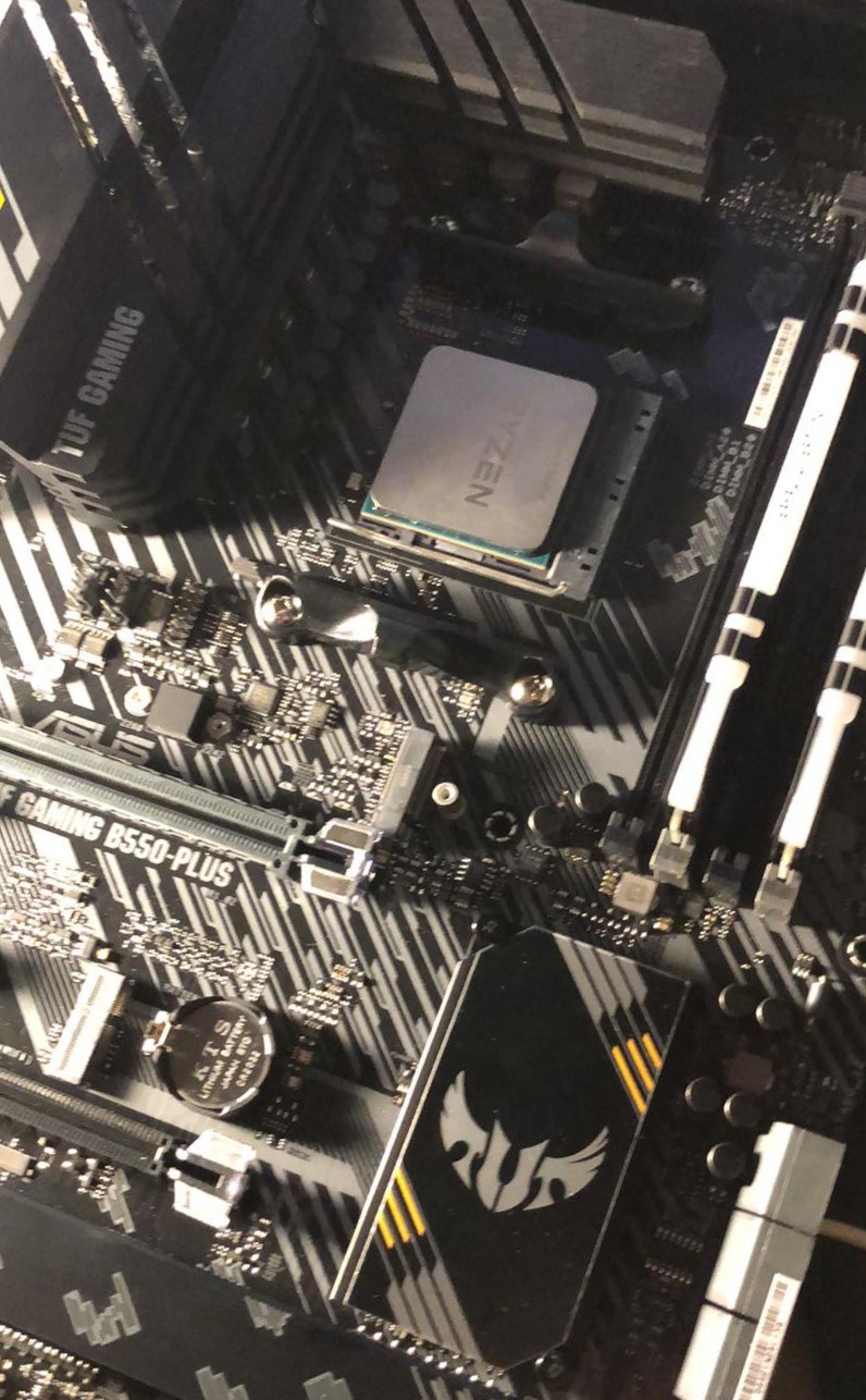 Płyta główna ASUS TUF GAMING B550-PLUS z zainstalowanym procesorem AMD Ryzen, widoczne gniazda pamięci RAM i bateria BIOS.