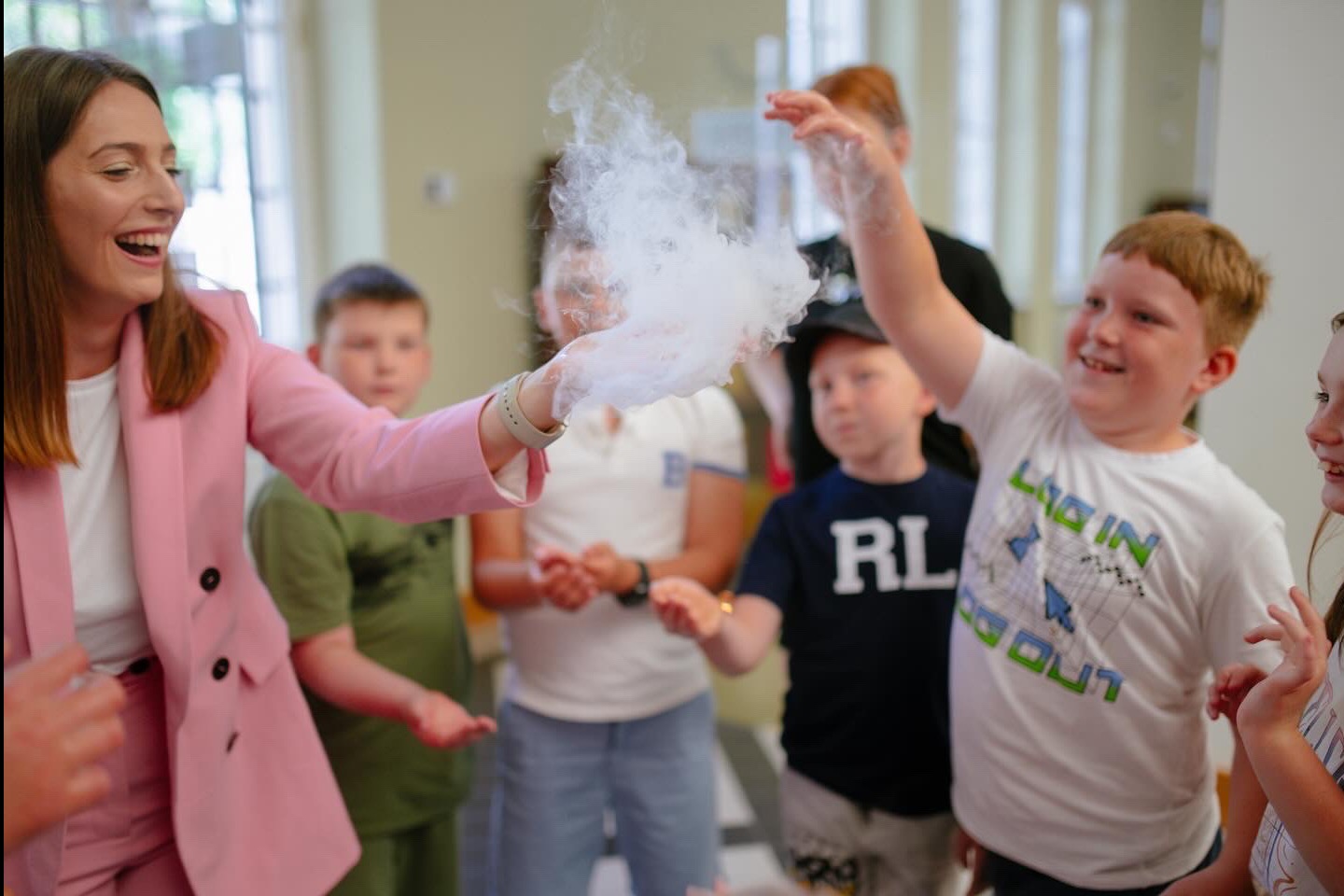 Animator w różowym żakiecie prezentuje dzieciom efektowny pokaz z dymem, wywołując uśmiechy i zaciekawienie podczas imprezy.