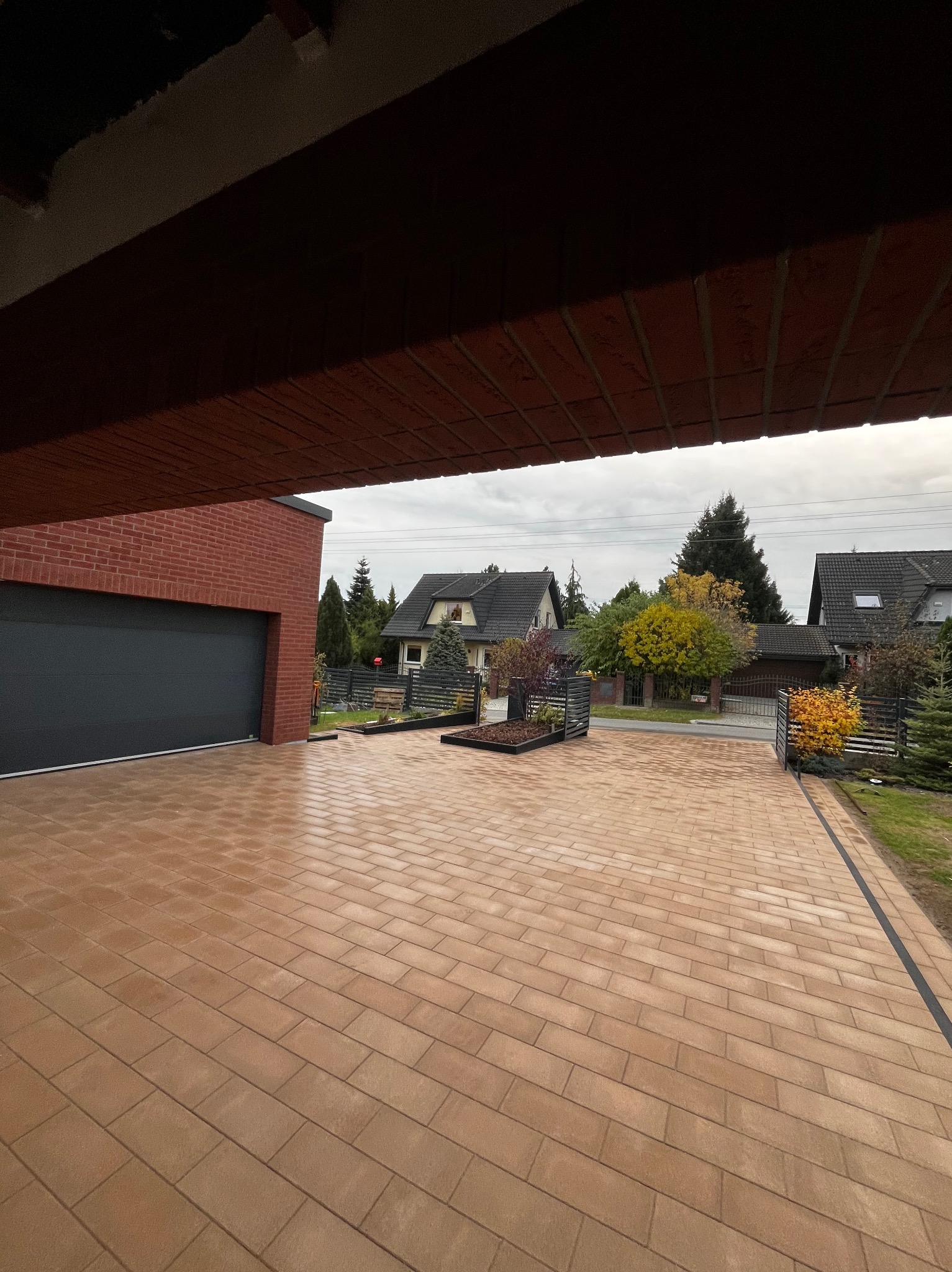 Nowa, brązowa kostka brukowa na podjeździe do garażu z cegły, widok z zadaszenia.