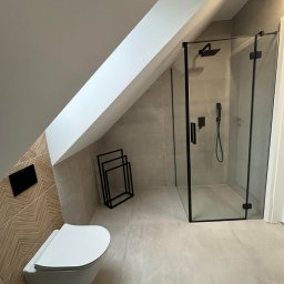 Grzegorz Podleszuk - Nowoczesna łazienka na poddaszu ze skośnym sufitem. Kabina prysznicowa z czarnymi ramami, podwieszana toaleta i dekoracyjna ściana z wzorem jodełki.