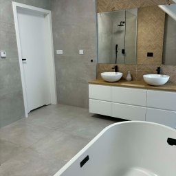 Grzegorz Podleszuk - Nowoczesna łazienka na poddaszu z szarą płytką, umywalkami nablatowymi i drewnopodobną mozaiką nad lustrem. Biała wanna wolnostojąca na pierwszym planie.