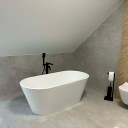 Grzegorz Podleszuk - Nowoczesna łazienka na poddaszu z wolnostojącą białą wanną i toaletą w stylu minimalistycznym. Szare płytki i drewnopodobne akcenty. Czarna armatura.