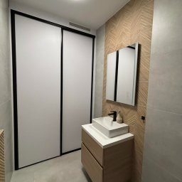 Grzegorz Podleszuk - Nowoczesna łazienka z umywalką nablatową, lustrem z podświetleniem LED i przesuwnymi drzwiami z czarnymi ramami. Ściana z dekoracyjną mozaiką w jodełkę.