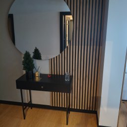 Grzegorz Podleszuk - Nowoczesny przedpokój z okrągłym lustrem, konsolą i lamelami na ścianie. Minimalistyczny design z akcentami dekoracyjnymi i ciepłym oświetleniem.