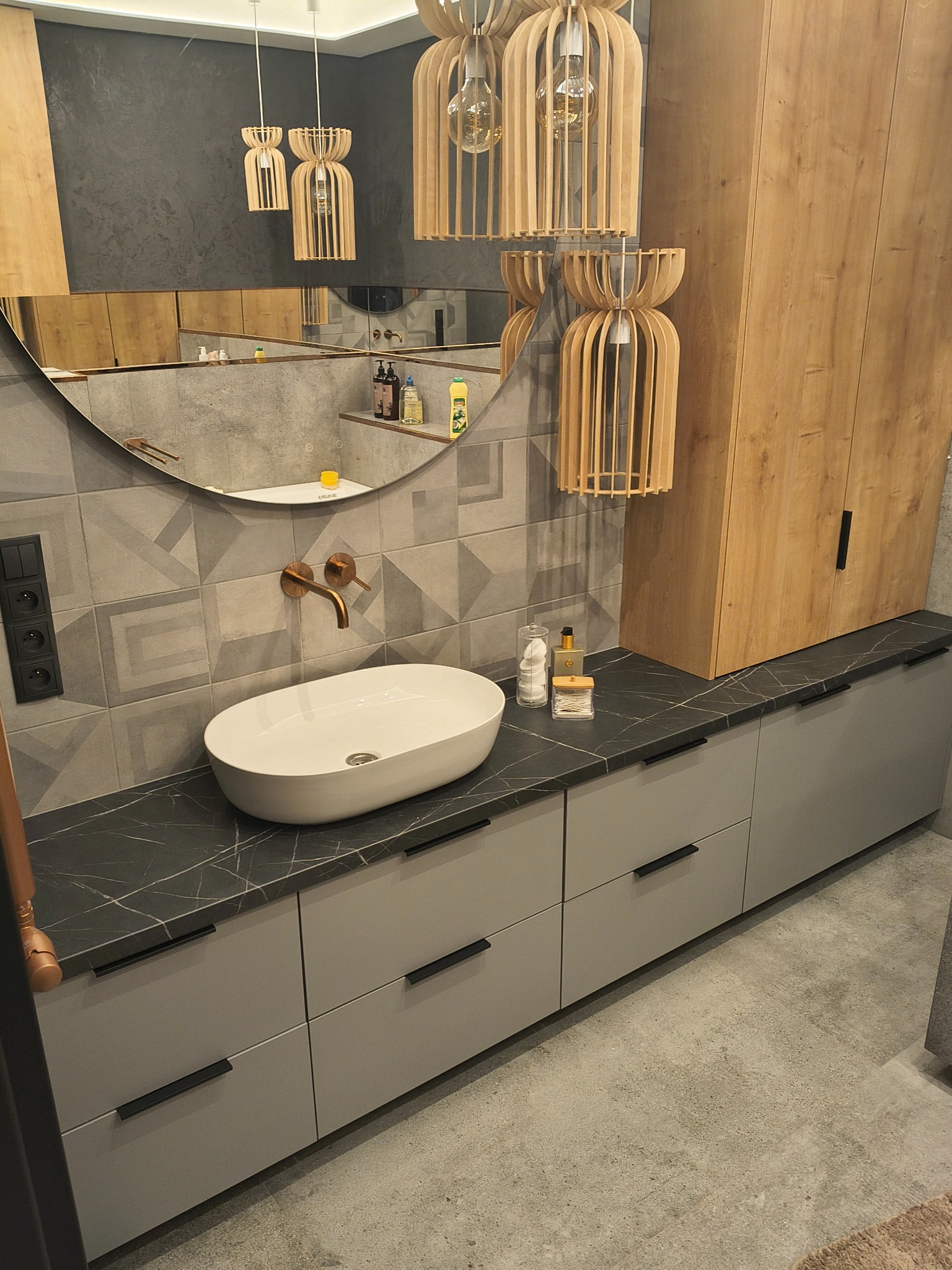Nowoczesna łazienka w Gorzowie Wielkopolskim: umywalka nablatowa, szara szafka z czarnym blatem, geometryczne płytki i drewniane lampy wiszące.