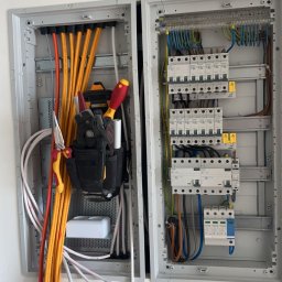 Leszek Lorek ELEKTRO-LO - Otwarta skrzynka elektryczna z przewodami, bezpiecznikami i narzędziami w kaburze po lewej stronie, widok z bliska na instalację elektryczną w trakcie prac.