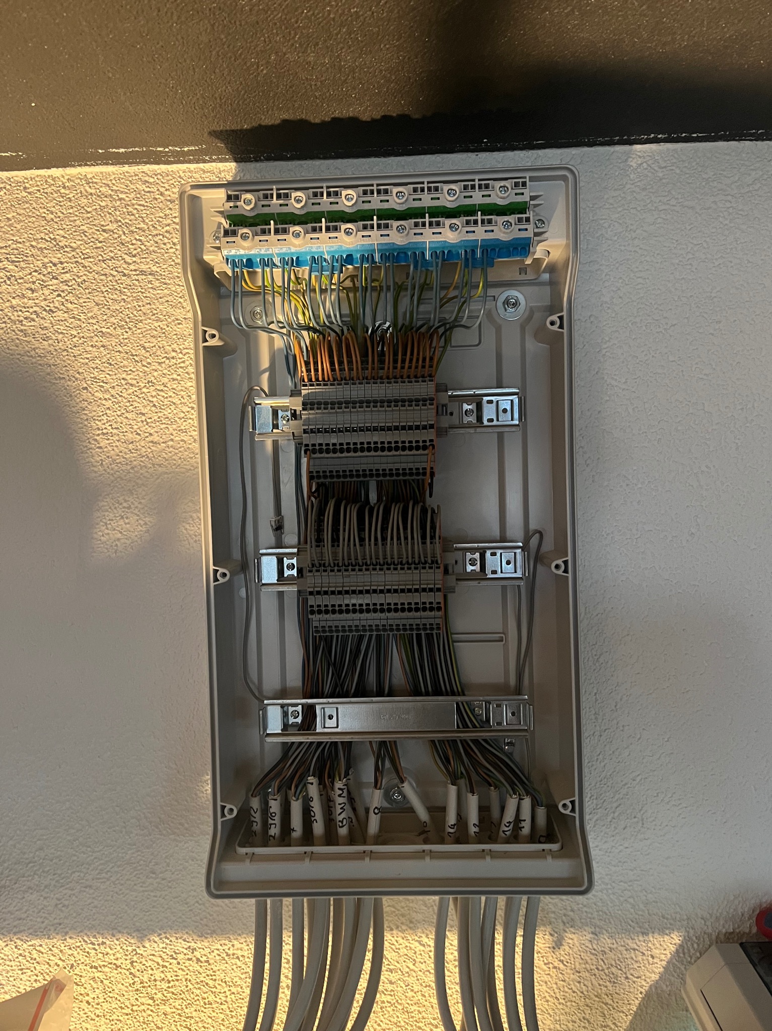 Otwarta skrzynka elektryczna z licznymi przewodami podłączonymi do listew zaciskowych, z widocznymi oznaczeniami na końcówkach przewodów.