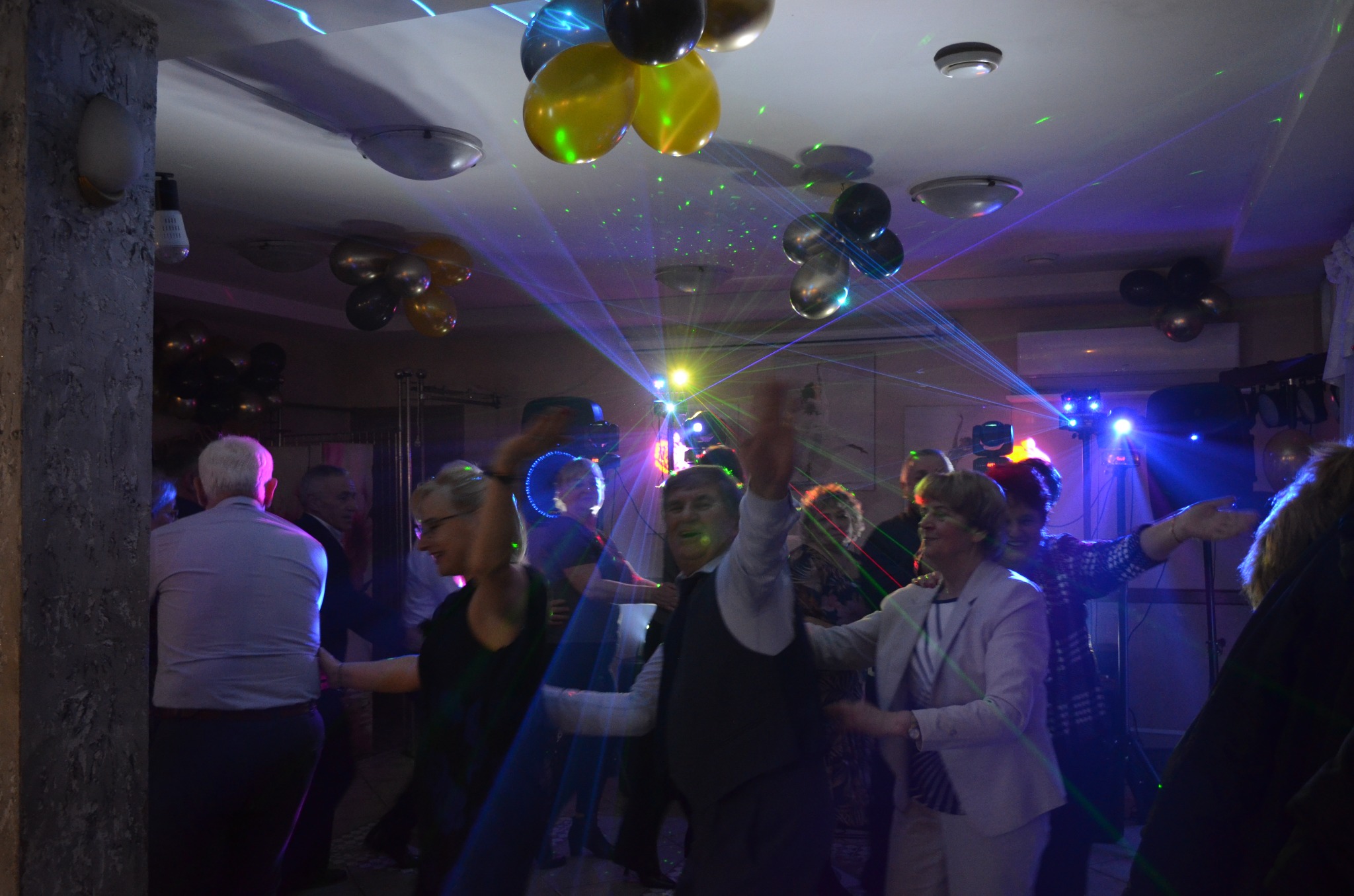 Klimatyzator ścienny widoczny w tle sali balowej, oświetlonej laserami i balonami, podczas imprezy tanecznej. Urządzenie wkomponowane w wystrój.