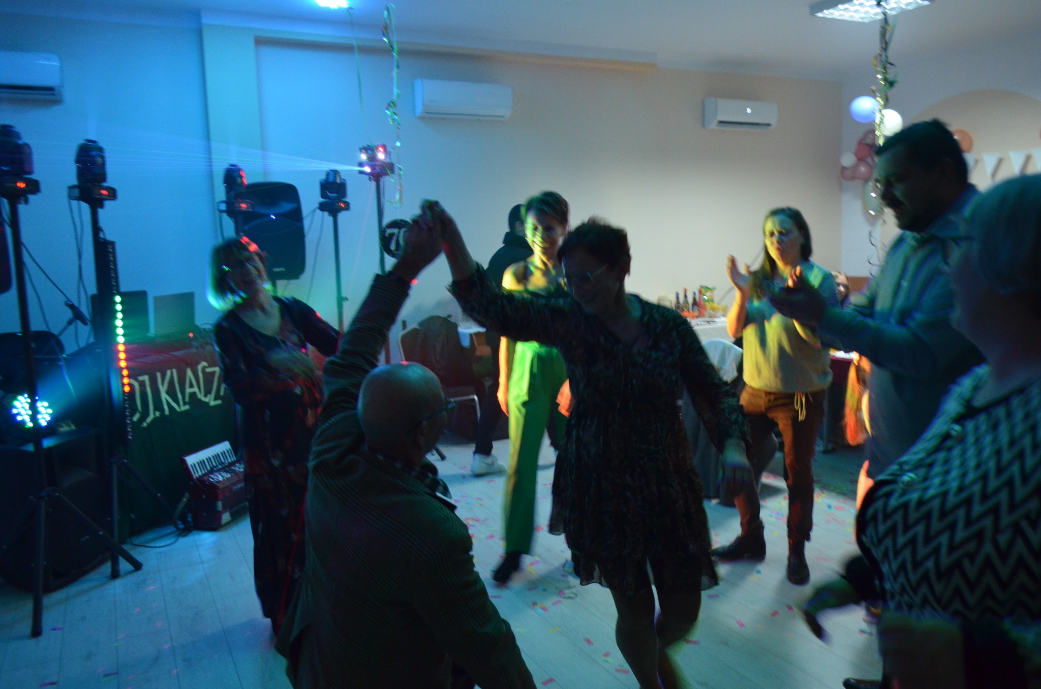 Zabawa taneczna w pomieszczeniu z klimatyzacją. W tle widoczne urządzenia klimatyzacyjne na ścianie. Oświetlenie dyskotekowe i dekoracje.