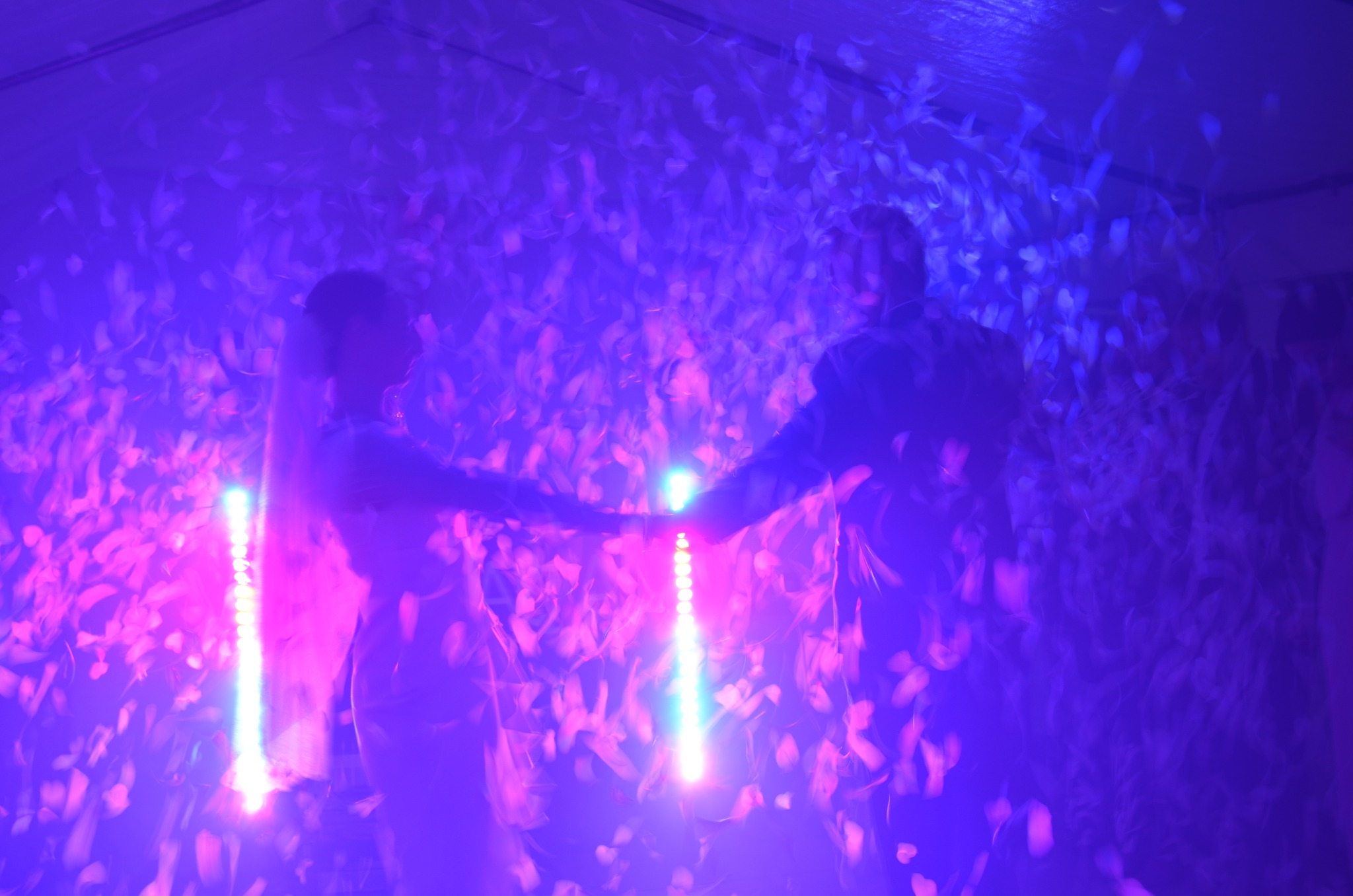 Para tańczy w strugach konfetti, oświetlona niebiesko-różowym światłem. Efektowne oświetlenie i opadające płatki tworzą magiczną atmosferę wydarzenia.