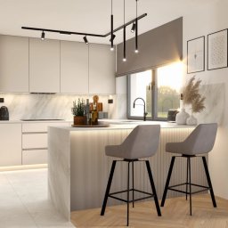 ENMAG.DESIGN Natalia Magiera - Nowoczesna kuchnia z wyspą, oświetleniem podszafkowym LED i dwoma szarymi hokerami przy wyspie. Na blacie dekoracje, a w tle trzy grafiki na ścianie.