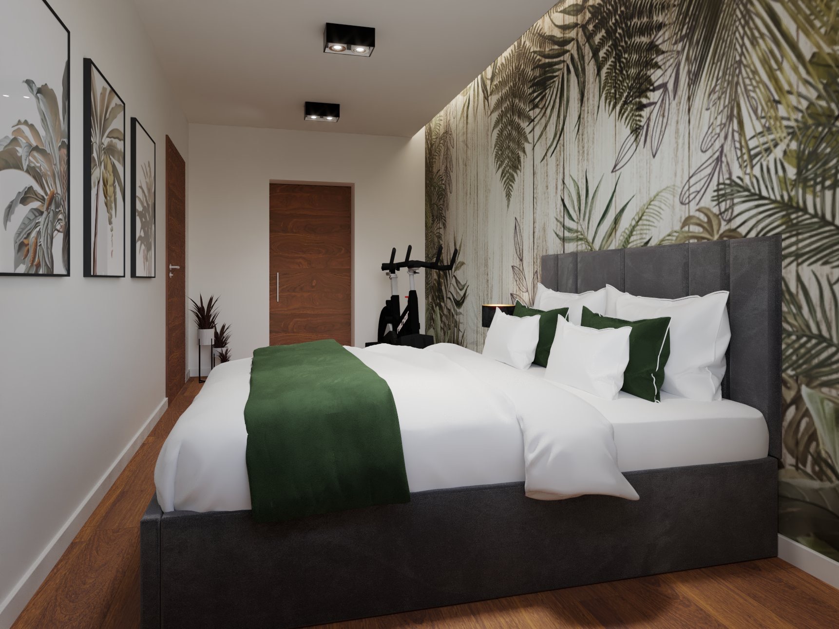 Sypialnia z łóżkiem kontynentalnym w szarej tapicerce, zielonym pledem i tapetą w motywy tropikalnych liści, z widocznym rowerem stacjonarnym w tle.