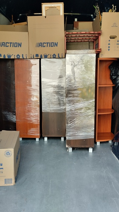 Meble zabezpieczone folią i kartony w przestrzeni ładunkowej pojazdu transportowego. Widoczne skrzynie marki Action. Przygotowanie do przeprowadzki.