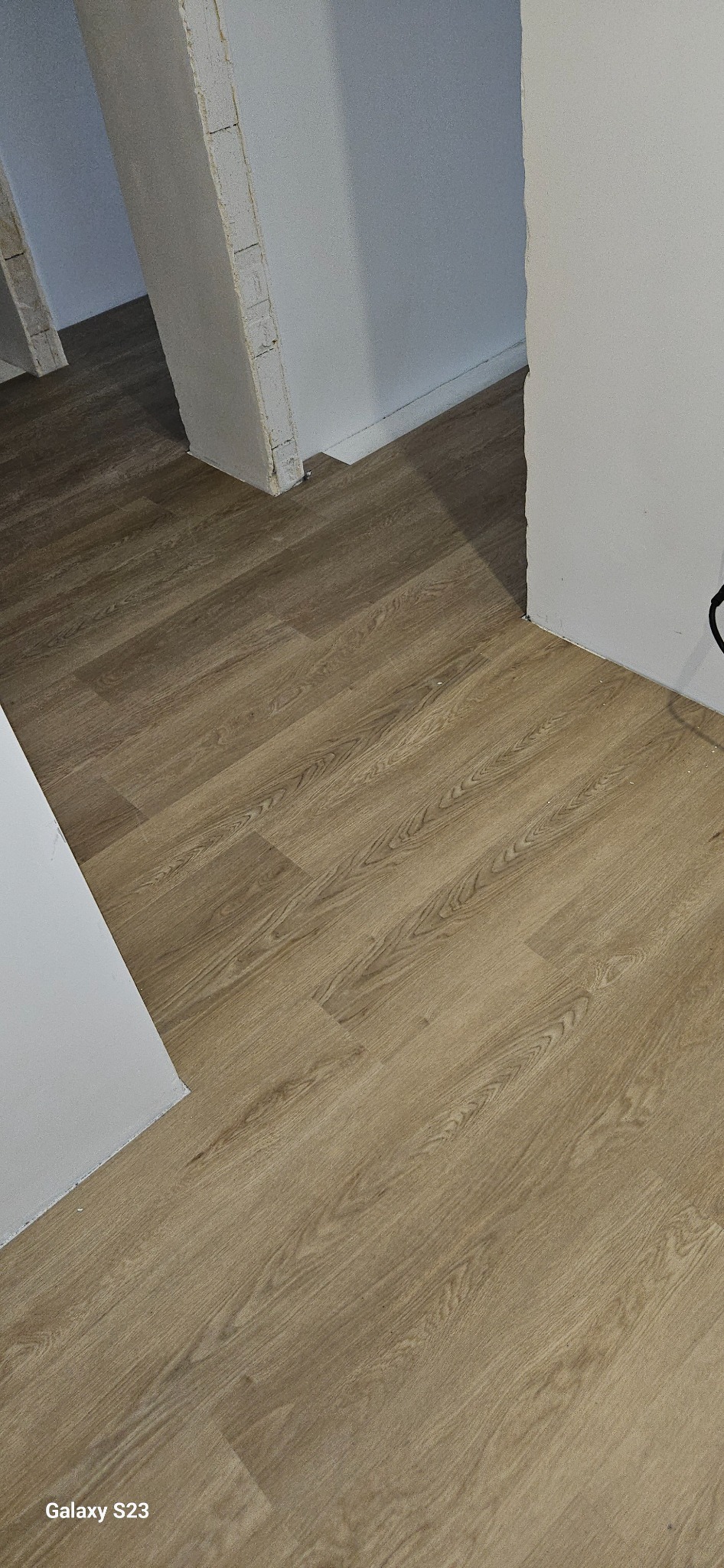 Ukończona podłoga z paneli laminowanych w odcieniach jasnego dębu, ułożona w nowym pomieszczeniu z surowymi ścianami, widoczne niedoskonałości wykończenia i ślady po remoncie.