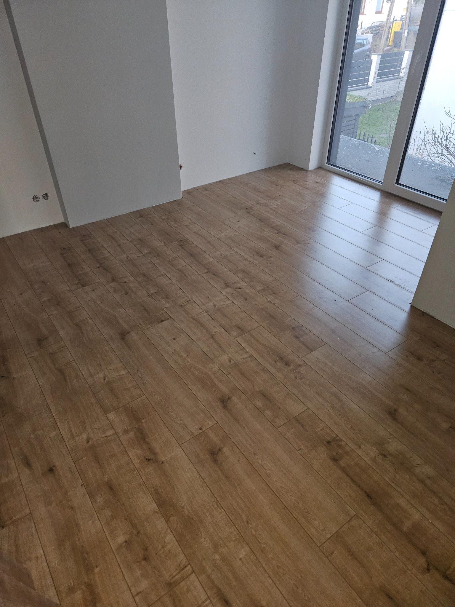 Nowo ułożona, jasnobrązowa podłoga laminowana w pustym pokoju z białymi ścianami i dużym oknem z widokiem na ulicę.