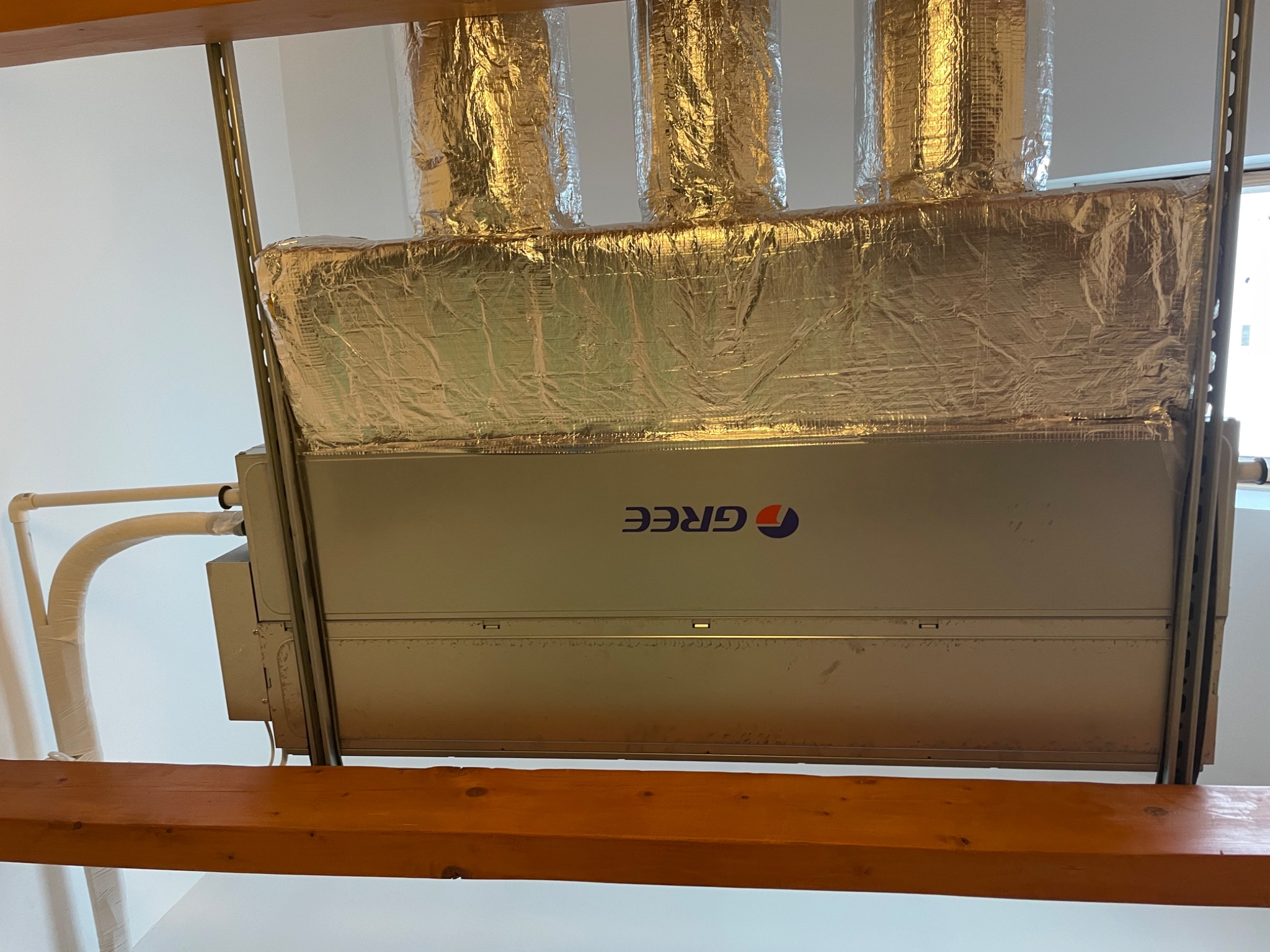 Klimatyzator marki GREE zamontowany pod sufitem, z izolowanymi przewodami wentylacyjnymi, widoczne elementy konstrukcji nośnej z drewna.