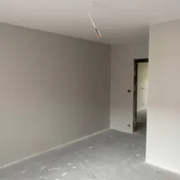 Świeżo pomalowane na szaro wnętrze z widoczną puszką farby na podłodze i wystającymi kablami z sufitu.