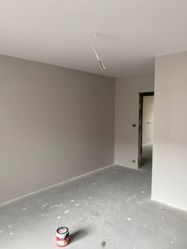 Świeżo pomalowane na szaro wnętrze z widoczną puszką farby na podłodze i wystającymi kablami z sufitu.