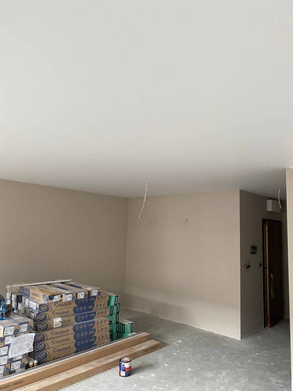 Przygotowane pomieszczenie do prac wykończeniowych: ściany w jasnym beżu, podłoga zabezpieczona folią, na podłodze ułożone paczki paneli podłogowych marki Barlinek i puszka farby.