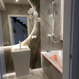 Katarzyna Zasadzińska Projekty Wnętrz - Nowoczesna łazienka z marmurowymi płytkami, owalnym lustrem z podświetleniem LED, wolnostojącą umywalką, białą armaturą i wanną zabezpieczoną folią ochronną podczas remontu.