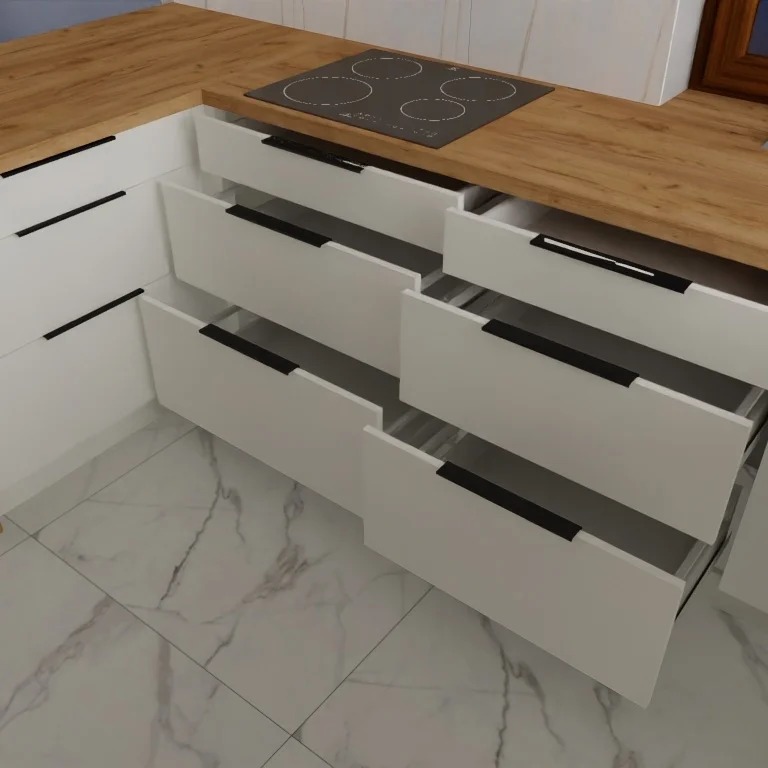 Białe szafki kuchenne z frontami bez uchwytów, z drewnianym blatem i płytą indukcyjną, kilka szuflad otwartych, marmurowe płytki na podłodze.