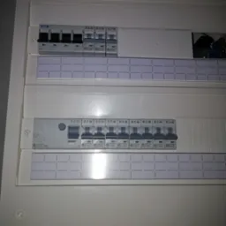 Otwarta skrzynka rozdzielcza z bezpiecznikami automatycznymi różnych typów i producentów, widoczne oznaczenia na obudowie i bezpiecznikach.