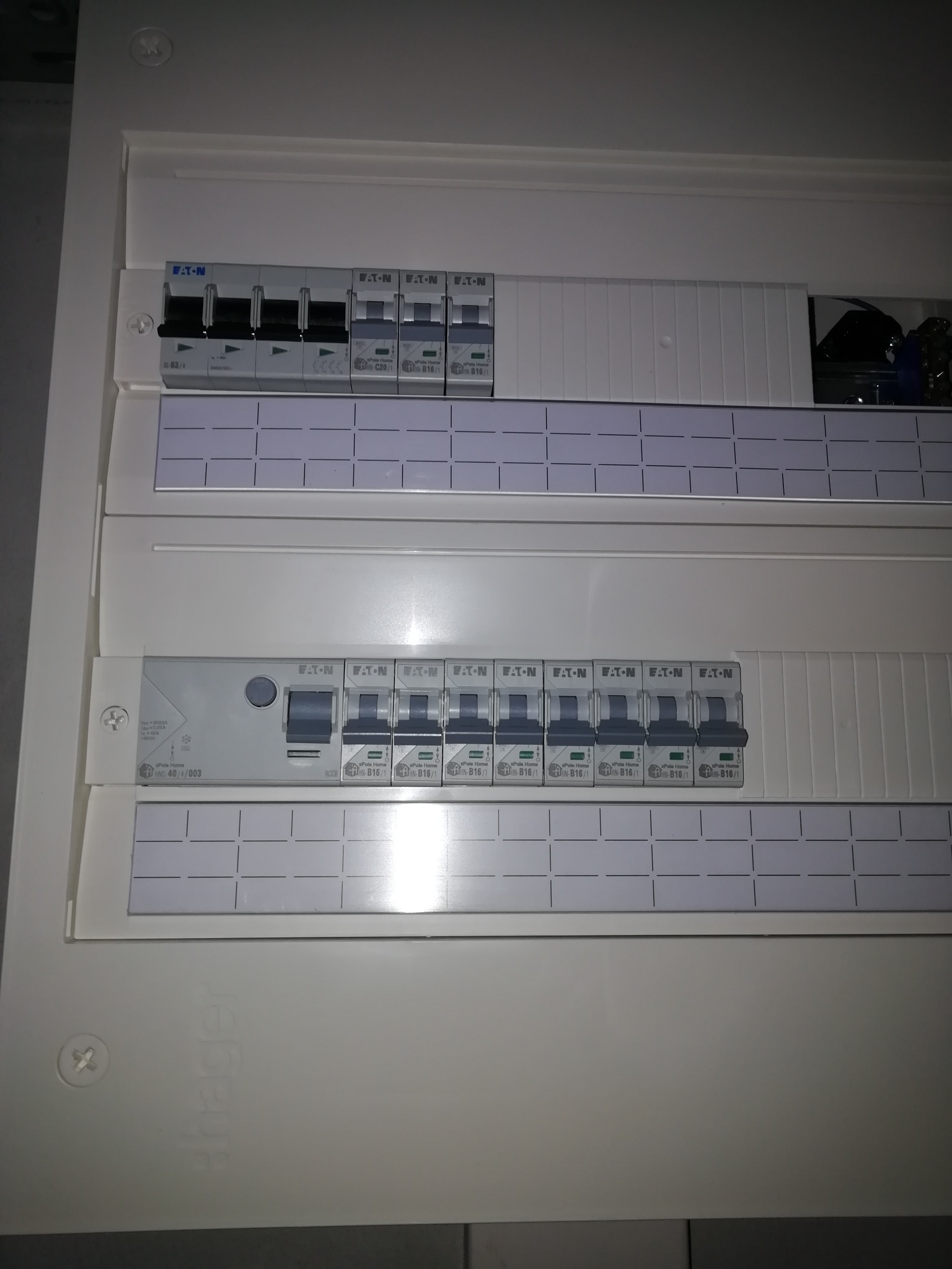 Otwarta skrzynka rozdzielcza z bezpiecznikami automatycznymi różnych typów i producentów, widoczne oznaczenia na obudowie i bezpiecznikach.