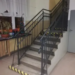 Wewnętrzne schody z metalową balustradą, zabezpieczone taśmą ostrzegawczą na krawędziach stopni, widok z dołu.