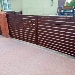 P&P FUH Przemyslaw Palega - Nowoczesna brama wjazdowa z poziomych, brązowych profili, zamontowana na ceglanych słupkach z kostką brukową na podjeździe.