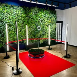 Instalacja do nagrywania filmów 360 stopni z tłem z żywych roślin, oświetleniem LED i czerwoną wykładziną, otoczona taśmą odgradzającą.