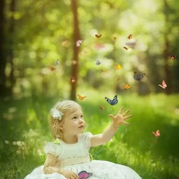 NAJKA SPÓŁKA Z OGRANICZONĄ ODPOWIEDZIALNOŚCIĄ - Mała dziewczynka w białej sukience siedzi na trawie, wyciągając rękę do motyli latających w powietrzu, z rozmytego tła leśnego.