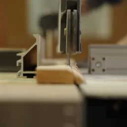 Piła taśmowa precyzyjnie tnąca drewniany element na stole warsztatowym, widoczne drobne wióry.