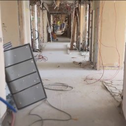 Efectivo Marek Pochylski - Korytarz w trakcie rozbiórki. Widoczne odsłonięte instalacje, gruz i pracownicy w oddali. Elementy konstrukcyjne budynku odsłonięte.