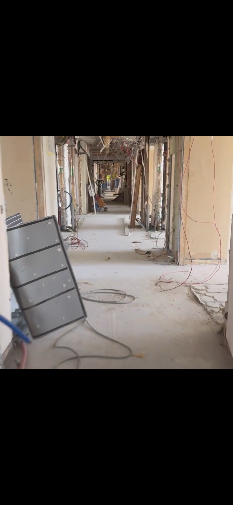 Korytarz w trakcie rozbiórki. Widoczne odsłonięte instalacje, gruz i pracownicy w oddali. Elementy konstrukcyjne budynku odsłonięte.