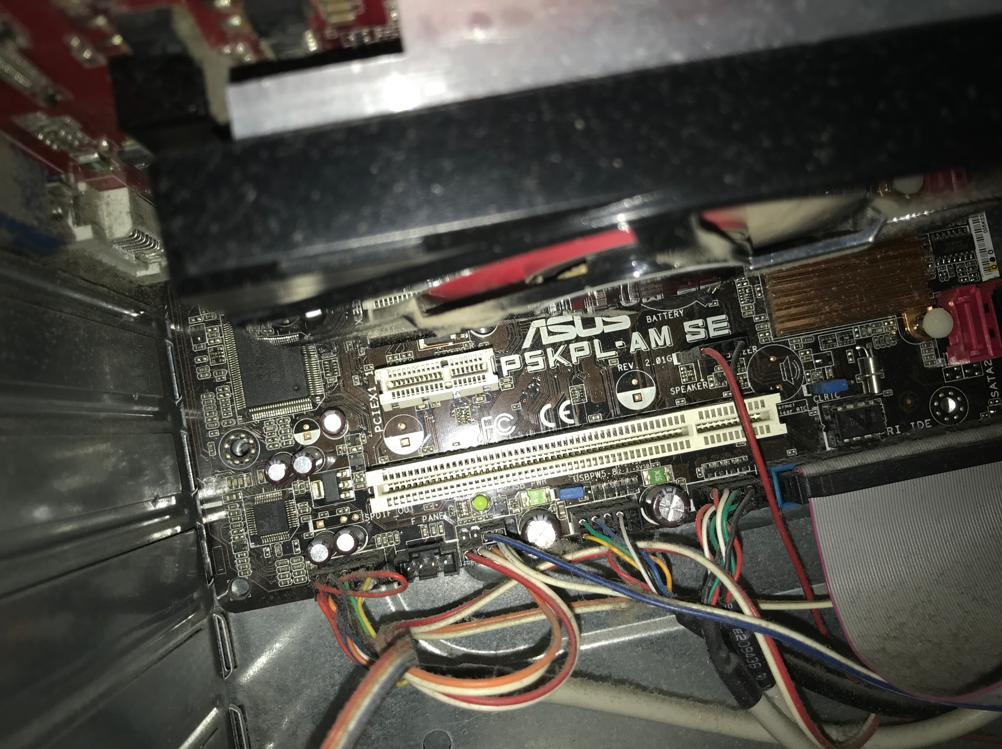 Wnętrze obudowy komputera stacjonarnego z widoczną płytą główną ASUS P5KPL-AM SE, licznymi przewodami i elementami chłodzenia, w warunkach słabego oświetlenia i widocznym kurzem.