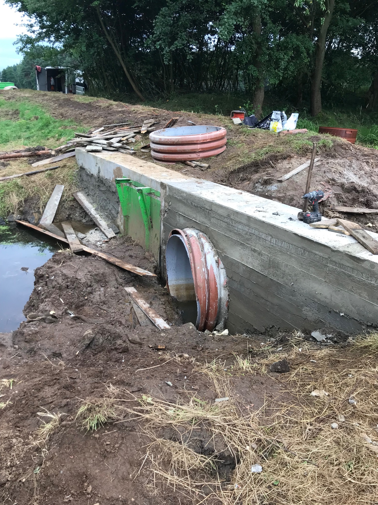 Budowa przepustu z rur betonowych i betonowej konstrukcji oporowej, widoczny wiertarko-wkrętak na górnej powierzchni konstrukcji.