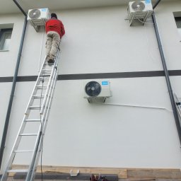 DMM Klimat Dawid Matejek - Montaż klimatyzacji Midea na elewacji domu. Instalator na drabinie przy urządzeniu, widoczna skrzynka z narzędziami. Dwa zamontowane klimatyzatory i jeden w trakcie montażu.