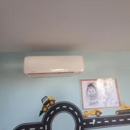 Biały klimatyzator Mitsubishi na błękitnej ścianie pokoju dziecięcego z dekoracjami drogowymi i rysunkami. Widok z dołu.