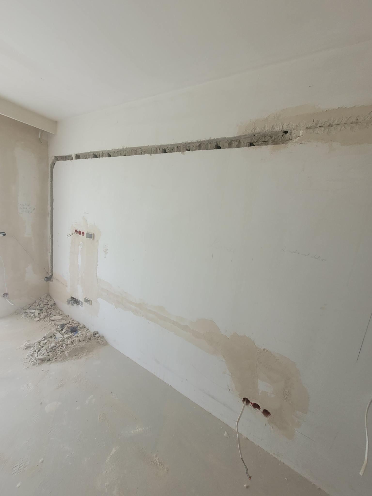 Przygotowanie pod montaż instalacji: wyżłobione bruzdy w ścianie pod przewody, widoczne puszki elektryczne z wystającymi kablami, gruz na podłodze.