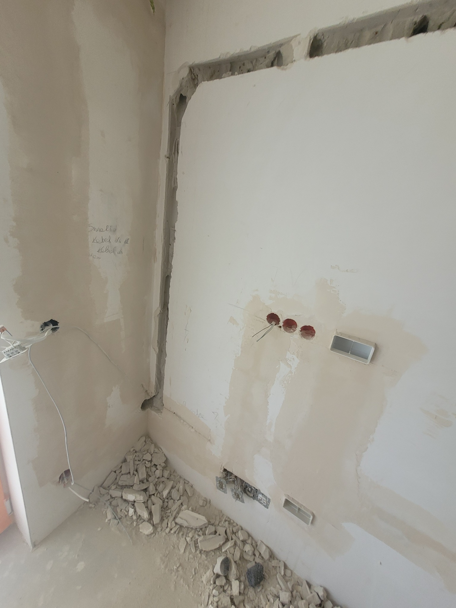 Przygotowania do instalacji w Łukowie: ściana z wyżłobieniami na kable i otwory pod gniazdka, gruz na podłodze, widoczne przewody elektryczne.
