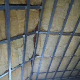 Poddasze z widoczną konstrukcją metalową i izolacją z wełny mineralnej, ujęcie z dołu pod kątem, widoczne niedoskonałości ściany bocznej.