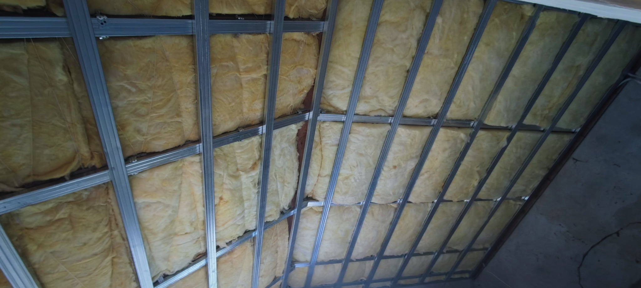 Poddasze z widoczną konstrukcją metalową i izolacją z wełny mineralnej, ujęcie z dołu pod kątem, widoczne niedoskonałości ściany bocznej.