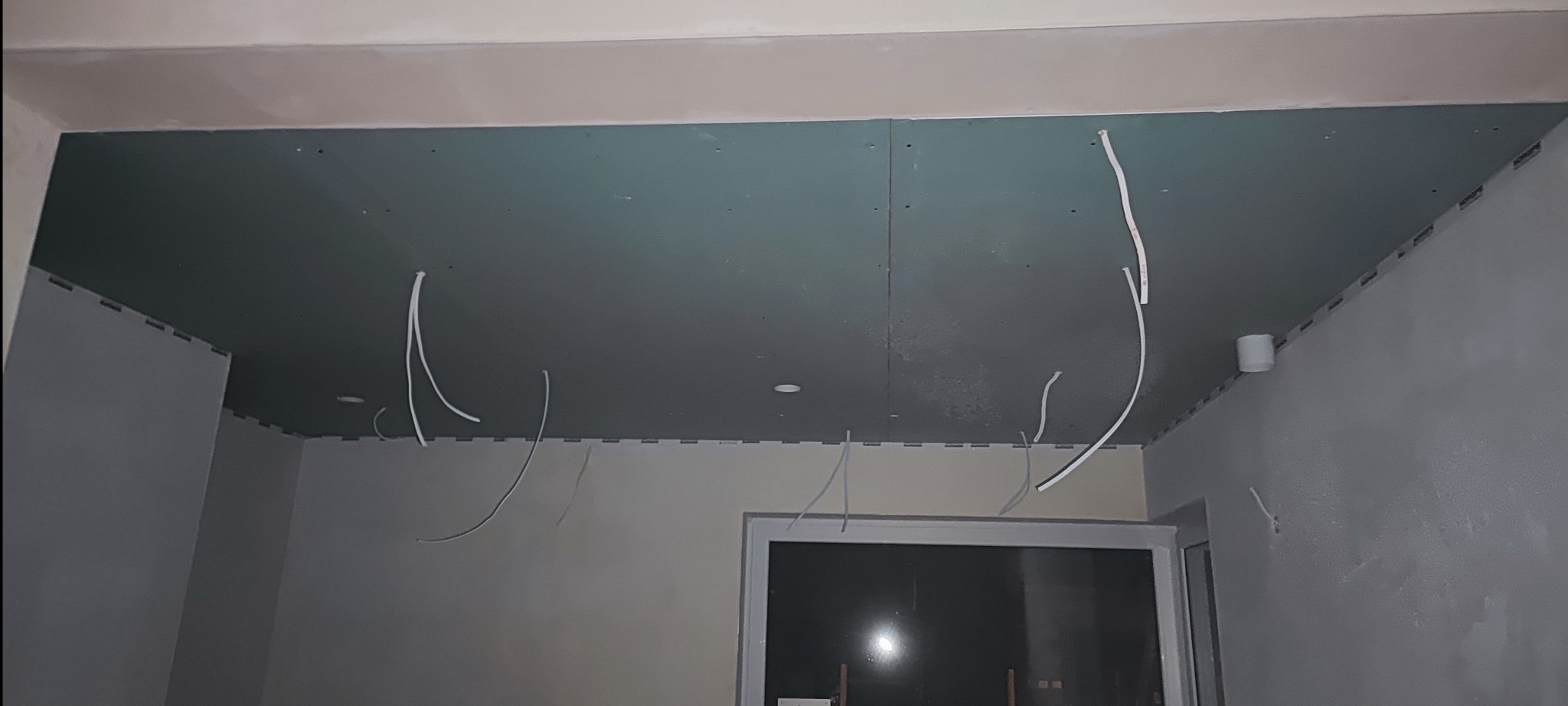 Montaż płyty karton gips na suficie z wystającymi przewodami elektrycznymi, widoczne profile mocujące i otwory na oświetlenie punktowe.