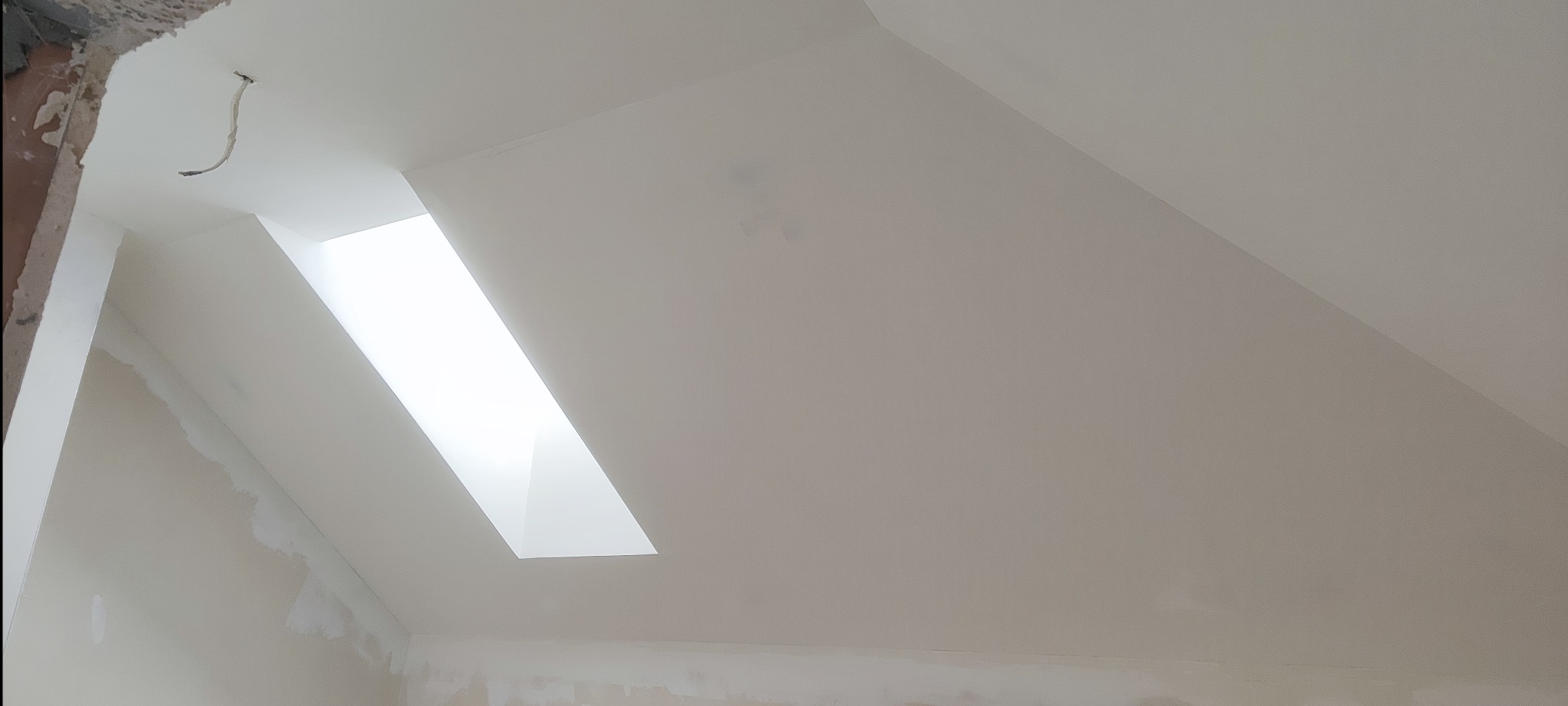 Poddasze z oknem dachowym po szpachlowaniu i malowaniu na biało, widoczne niedoskonałości i ślady po taśmie malarskiej.